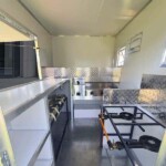 View inside a customizable food truck featuring gas stoves, fryers, and stainless steel countertops